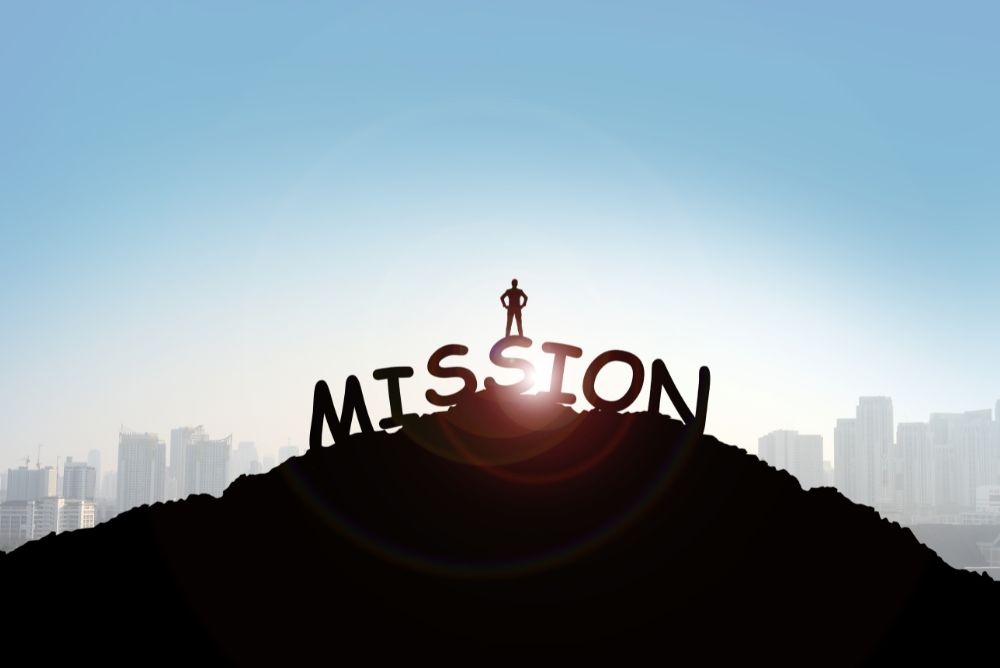 Person standing on top of the board which says "MISSION".